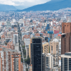 Vista panorámica del centro de Bogotá con edificios de gran altura, zonas residenciales densamente construidas y montañas al fondo bajo cielo parcialmente nublado.