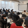 Foto que muestra personas sentadas en escritorios en un salón de clases