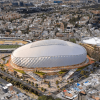 Vista aérea de un estadio cubierto de forma ovalada, rodeado por vías, edificaciones y zonas urbanas densamente construidas.