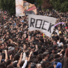 Multitud de asistentes reunidos al aire libre durante Rock al Parque en Bogotá. En el centro se observa una bandera blanca con la palabra “ROCK”, mientras cientos de personas ocupan gran parte del espacio frente al escenario, rodeadas por árboles.