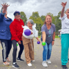 Grupo de personas participa en una actividad recreativa al aire libre; varias sostienen pelotas mientras avanzan por una zona verde.