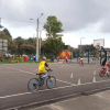 Persona con casco amarillo monta una bicicleta entre conos de señalización instalados en una pista durante Vacaciones Recreativas del IDRD con actividades de formación ciclista al aire libre.